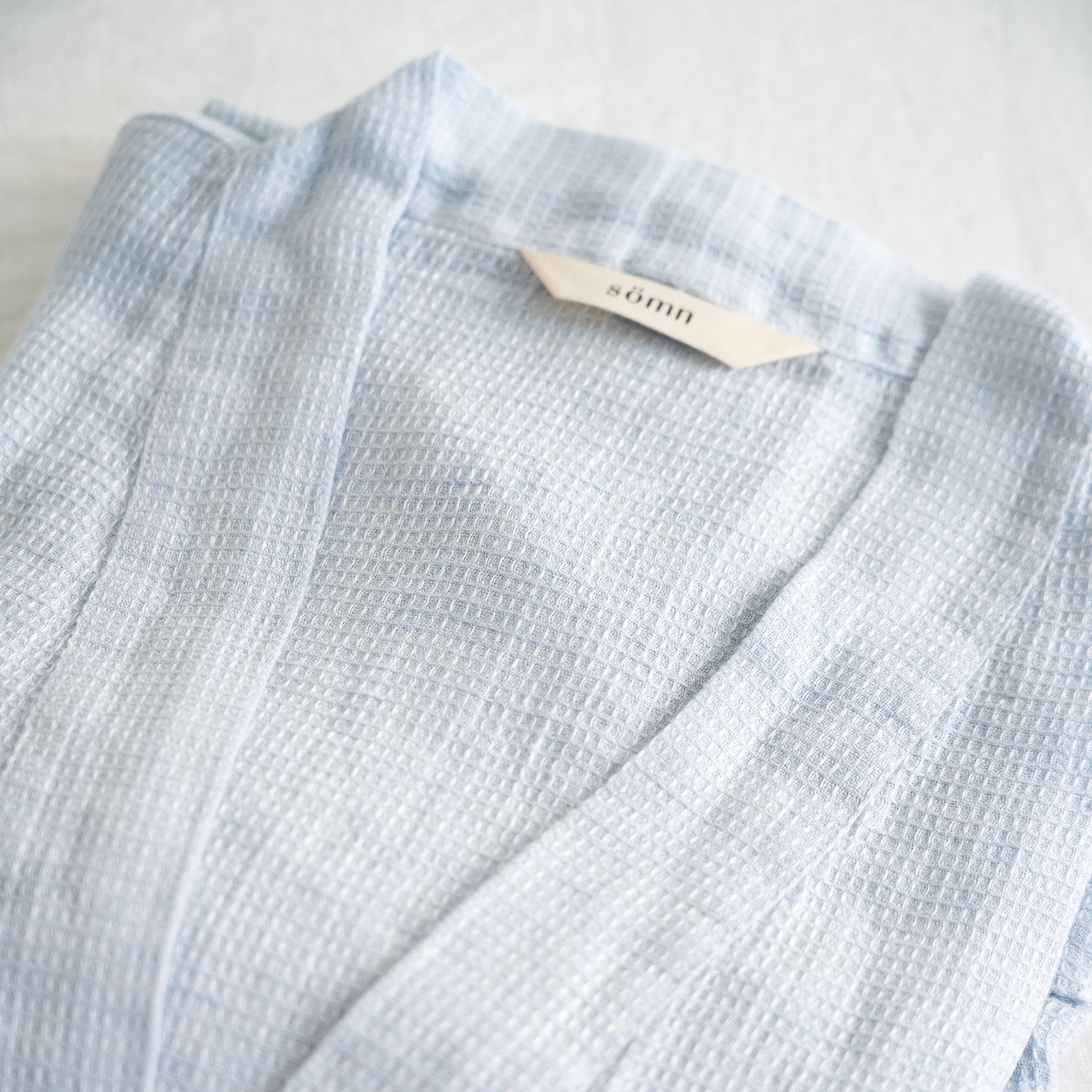 A detail picture of the waffle bathrobe with Sömn hang tag #color_opal-sky